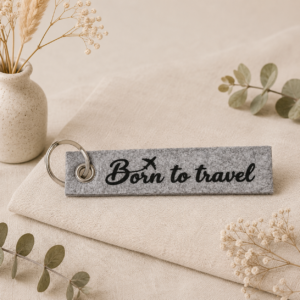 Grauer Filz-Schlüsselanhänger mit Schriftzug "Born to travel" und Flugzeug-Symbol, dekoriert mit getrockneten Blumen