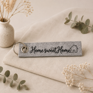 Grauer Filz-Schlüsselanhänger mit Schriftzug "Home sweet Home" und Haus-Symbol, dekoriert mit getrockneten Blumen
