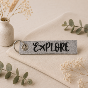Grauer Filz-Schlüsselanhänger mit Schriftzug "Explore" und Flugzeug-Symbol, dekoriert mit getrockneten Blumen